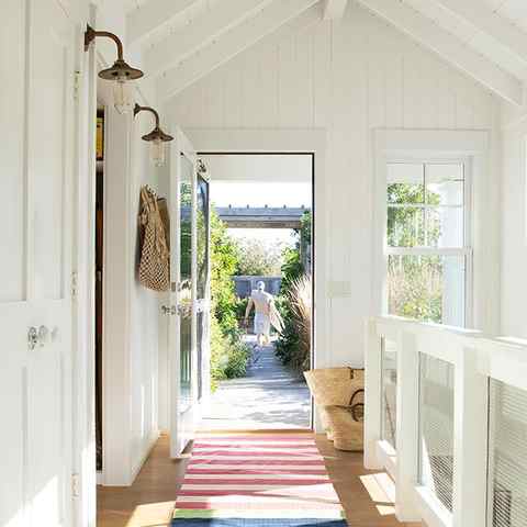 A beach house entryway with off-white-painted walls, wired railing, striped runner, and light wood floor.