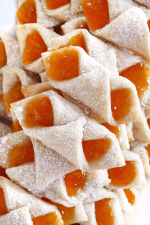 A white plate with apricot jam filled kolaczki (or kolacky) Polish cookies topped with powdered sugar.