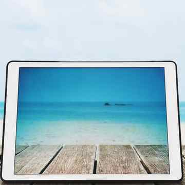 digital tablet with sunglasses on wooden desk at tropical beach