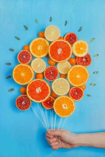 A still life photography arrangement of oranges made to look like a bunch of balloon on a blue background 