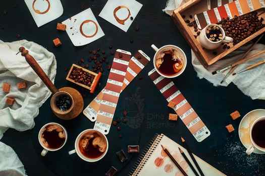Overhead still life shot of coffee items, color swatches, pencils and a sketchpad on a dark background