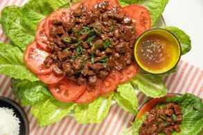 Platter of Lok Lak Served Over Sliced Tomatoes and Lettuce at a Table Setting With a Bowl of Rice, a Plate With a Serving of Lok Lak, and a Bowl of Pepper-lime Sauce 