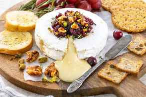 Baked brie with cranberry sauce and candied walnuts on a serving tay with crackers and fruit set around it.