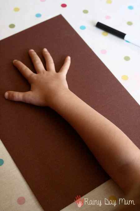 toddler placing hand on brown paper to draw around and create a tree trunk