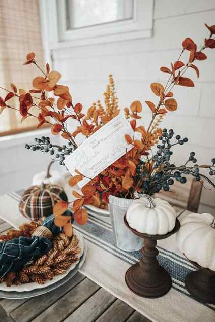 an all-natural fall centerpiece of a planter with berries, bright leaves on branches and faux pumpkins on stands