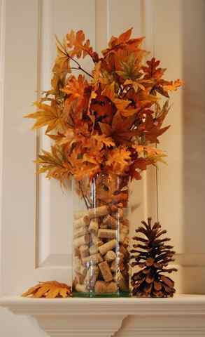 a simple fall centerpiece of a glass vase with wine corks and fall leaves on branches can be DIYed fast